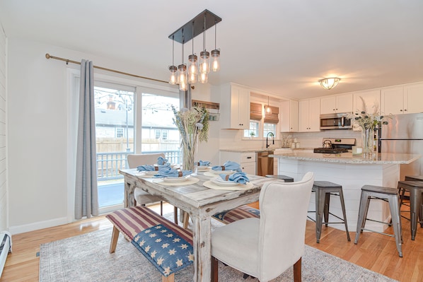 A modern kitchen with white cabinets, stainless steel appliances, and a dining area with a wooden table and bar stools.