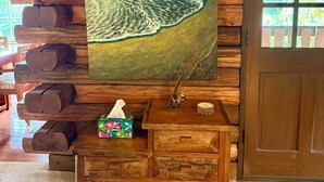 Ein Holzblockhaus-Interieur mit einem großen Gemälde vom Strand, einer Holzbank und einem kleinen Holztisch mit einer Taschentuchbox.