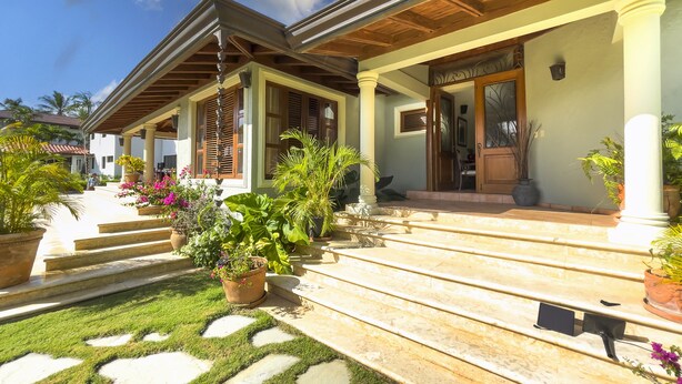 A two-story house with a covered porch, steps leading to the entrance, and potted plants.