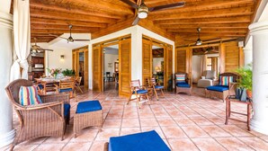 A spacious patio with wicker furniture, wooden ceiling beams, and tiled flooring.