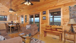 L’intérieur chaleureux d’un chalet avec des murs en bois, un coin repas, un salon doté d’un canapé et d’un banc, et un balcon offrant une vue imprenable.
