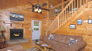 L’intérieur d’un chalet en bois, avec une cheminée, un canapé, une table basse et un escalier.