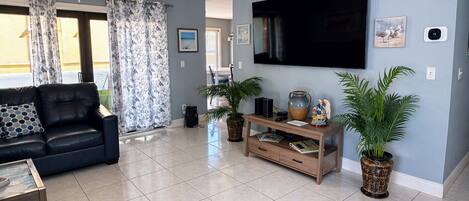 A living room with a black leather sofa, a wooden TV stand with a flat-screen TV, and two potted plants.