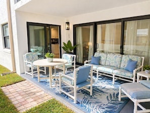 A patio with a white table, chairs, and a sofa with blue cushions.