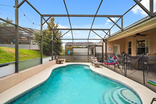 A covered outdoor swimming pool with a glass enclosure, surrounded by chairs and a slide.