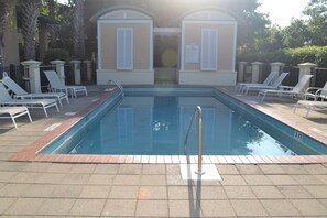 Une piscine rectangulaire avec un escalier en métal, entourée de chaises longues blanches et bordée de briques.