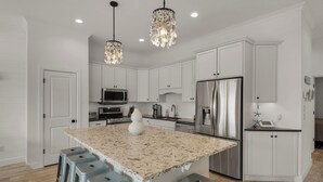 Una cocina moderna con armarios blancos, una isla grande con taburetes de bar, electrodomésticos de acero inoxidable y una lámpara de techo original.