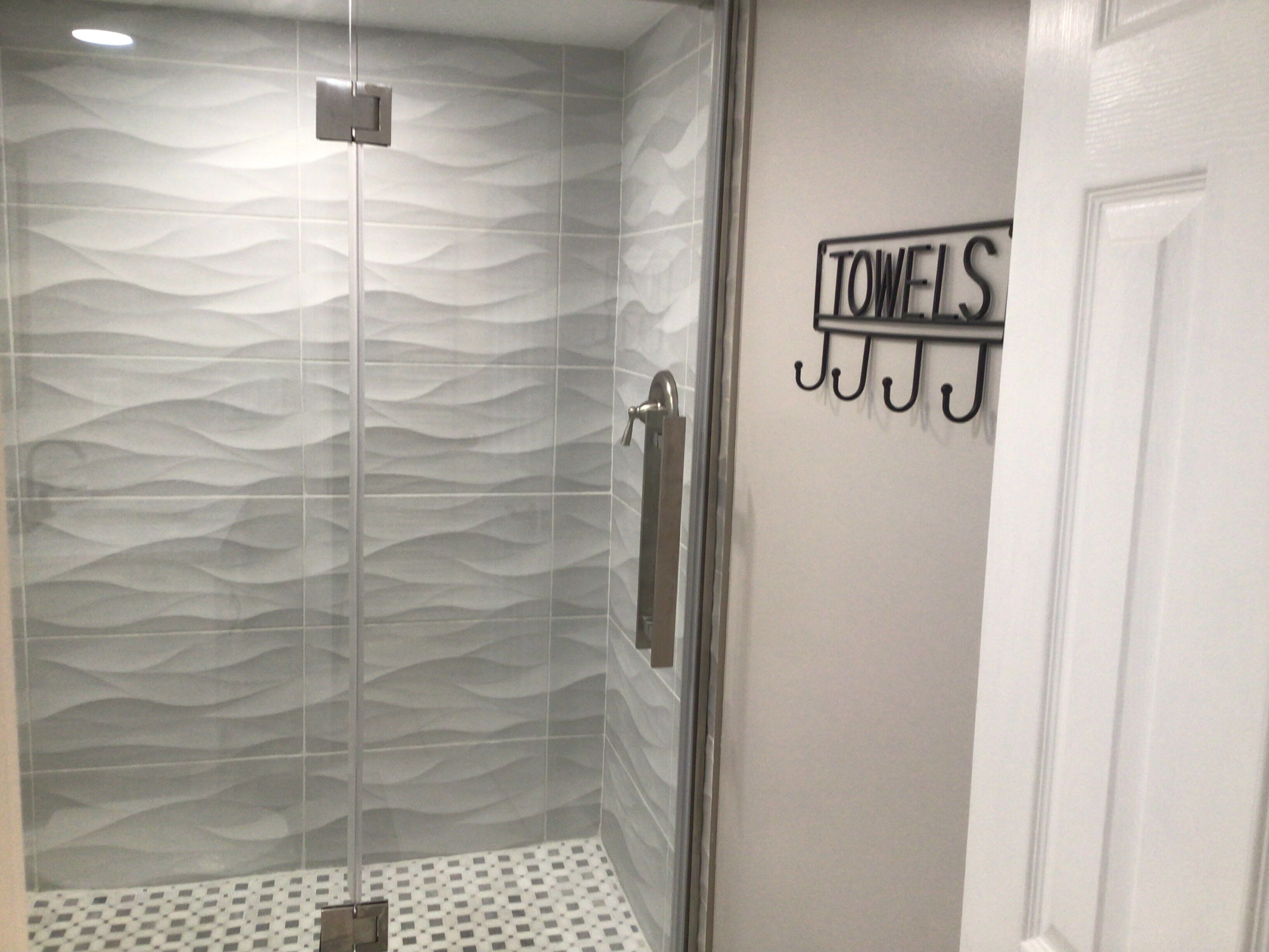 A bathroom with a textured shower wall, a towel rack, and a patterned floor.