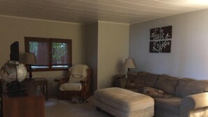 A living room with a beige carpet, a wooden chair, a sofa, a small table with a globe, and a window with blinds.