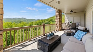 A covered porch with a stone pillar, wicker furniture, and a view of green hills. - Panoramic Luxury Retreat with Mountain View’s (Banner Elk)
