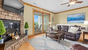 A living room with a fireplace, leather sofa, and a ceiling fan. - Panoramic Luxury Retreat with Mountain View’s (Banner Elk)