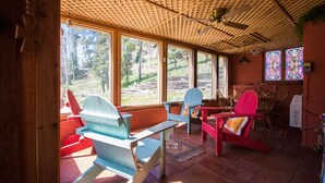 Een rustieke hut met houten balkenplafond, grote ramen en Adirondack stoelen.