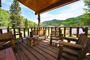Terraza de madera con mesa y sillas, con vistas a una zona montañosa boscosa.