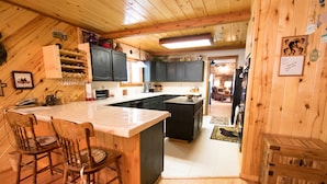 Een keuken met houten kasten, een groot eiland met barkrukken en uitzicht op de eetruimte.