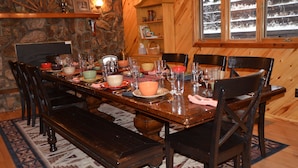 Een houten eettafel gedekt met borden, kommen en glazen, omringd door stoelen, in een kamer met stenen muren en een raam met uitzicht.