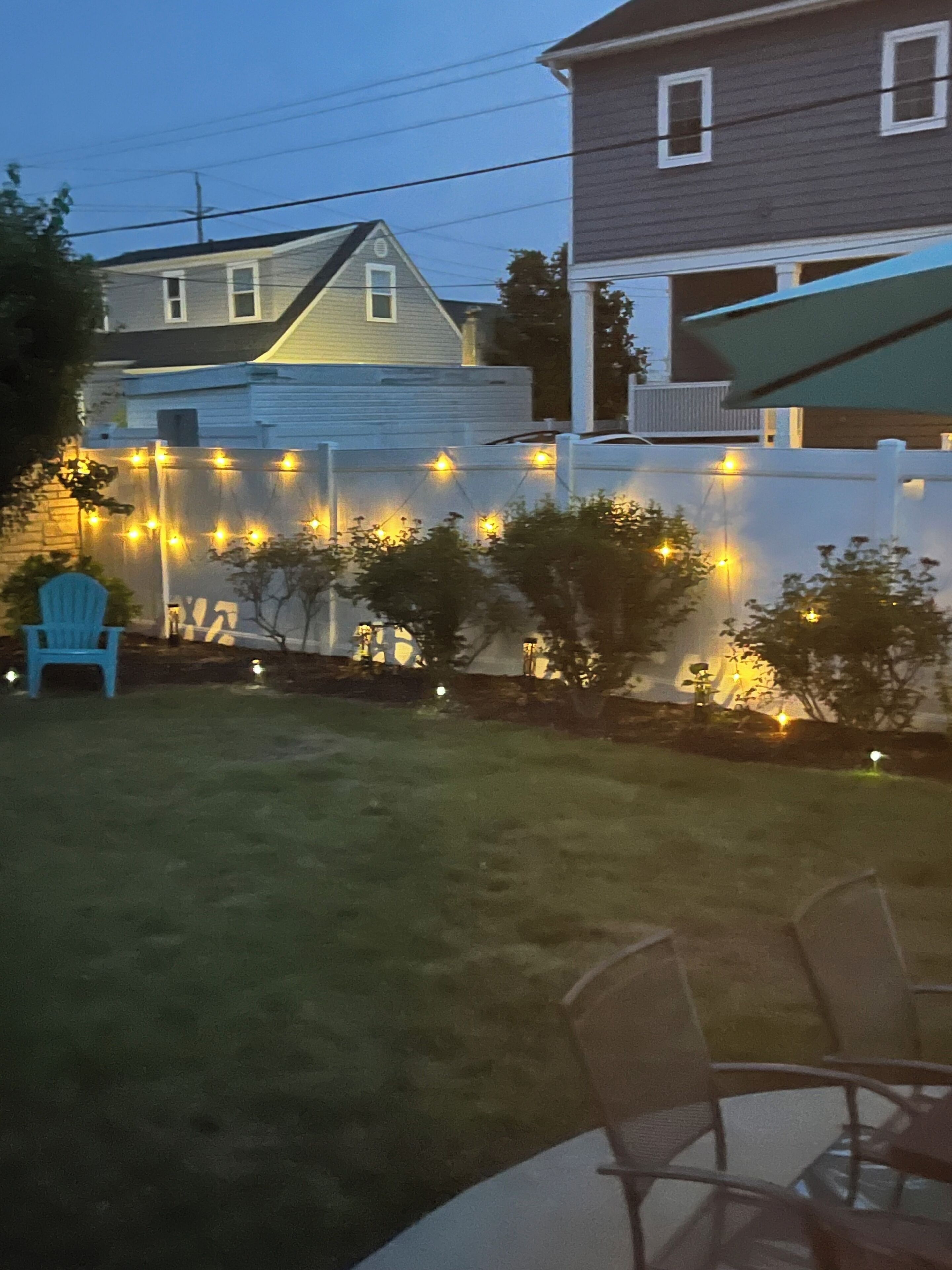 Ein Garten mit weißem Zaun, Lichterketten, einem blauen Stuhl und einem Tisch.