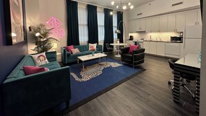 A modern living room with a sofa, coffee table, and chairs, a kitchen with white cabinets, and a dining area with a table and chairs.
