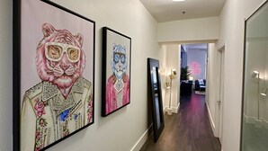 A hallway with framed artwork on the walls, a modern light fixture, and a view into another room.