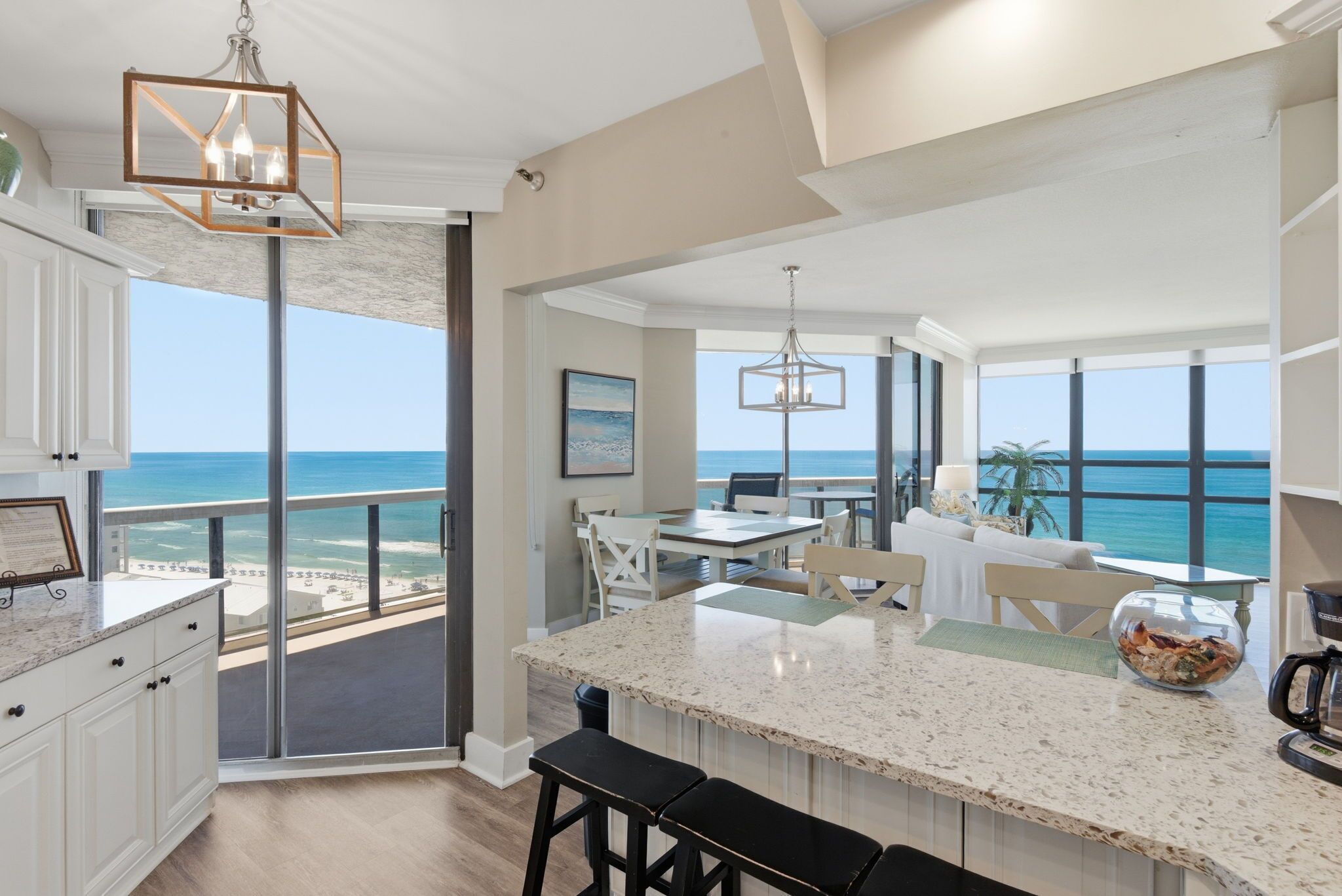 A modern kitchen with a large island, a dining area with a view of the ocean, and a spacious living area with a balcony overlooking the beach.
