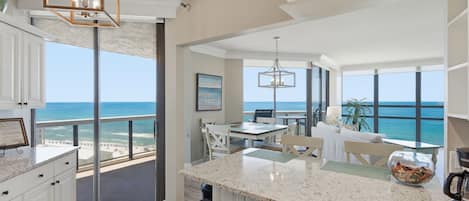 A modern kitchen with a large island, a dining area with a view of the ocean, and a spacious living area with a balcony overlooking the beach.