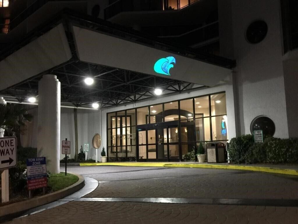 A hotel entrance with a prominent logo above the doors, a one-way sign, and a tow-away zone sign.