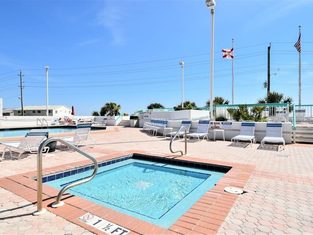 A swimming pool area with lounge chairs, a pool ladder, and a flagpole with flags.