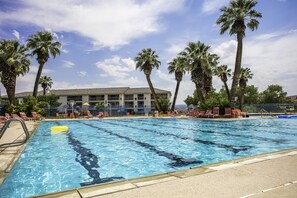 Una piscina con acqua cristallina e blu, circondata da palme e un edificio con numerose finestre sullo sfondo.