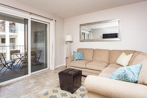 Un salon avec un canapé beige, une table basse et une porte vitrée donnant sur un espace extérieur doté d’un balcon.