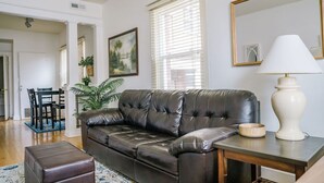 A living room with a leather sofa, a dining table with chairs, and a large window with blinds. - Quaint Downtown Condo (Salt Lake City)