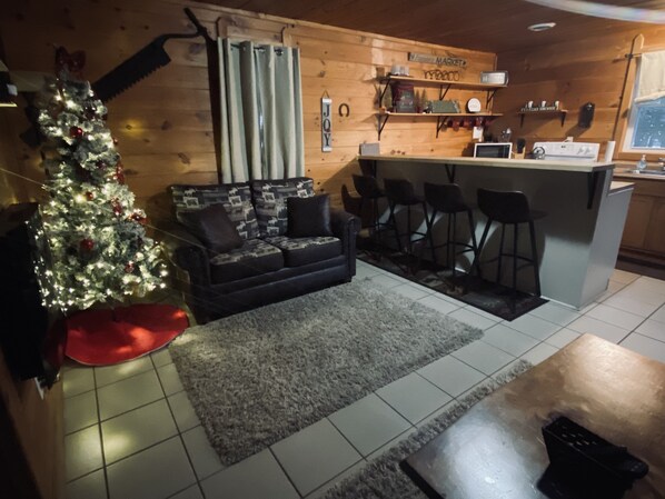 A cozy living room with a Christmas tree, a sofa, and a kitchen area with a bar.