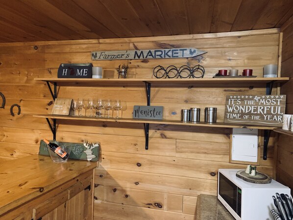 A wooden interior with shelves displaying various items, including wine glasses, a sign reading "It's the most wonderful time of the year," and a sign that says "Farmer's Market."