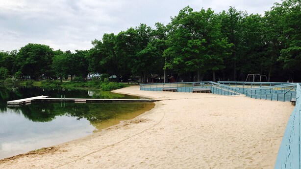 A sandy beach with a dock extending into a calm body of water, surrounded by trees. - 3 Bed Cozy Cabin Near Trails, Tippy Dam, Manistee River, Casino. (Wellston)
