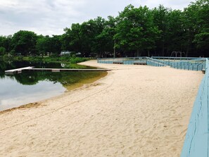 A sandy beach with a dock extending into a calm body of water, surrounded by trees. - 3 Bed Cozy Cabin Near Trails, Tippy Dam, Manistee River, Casino. (Wellston)