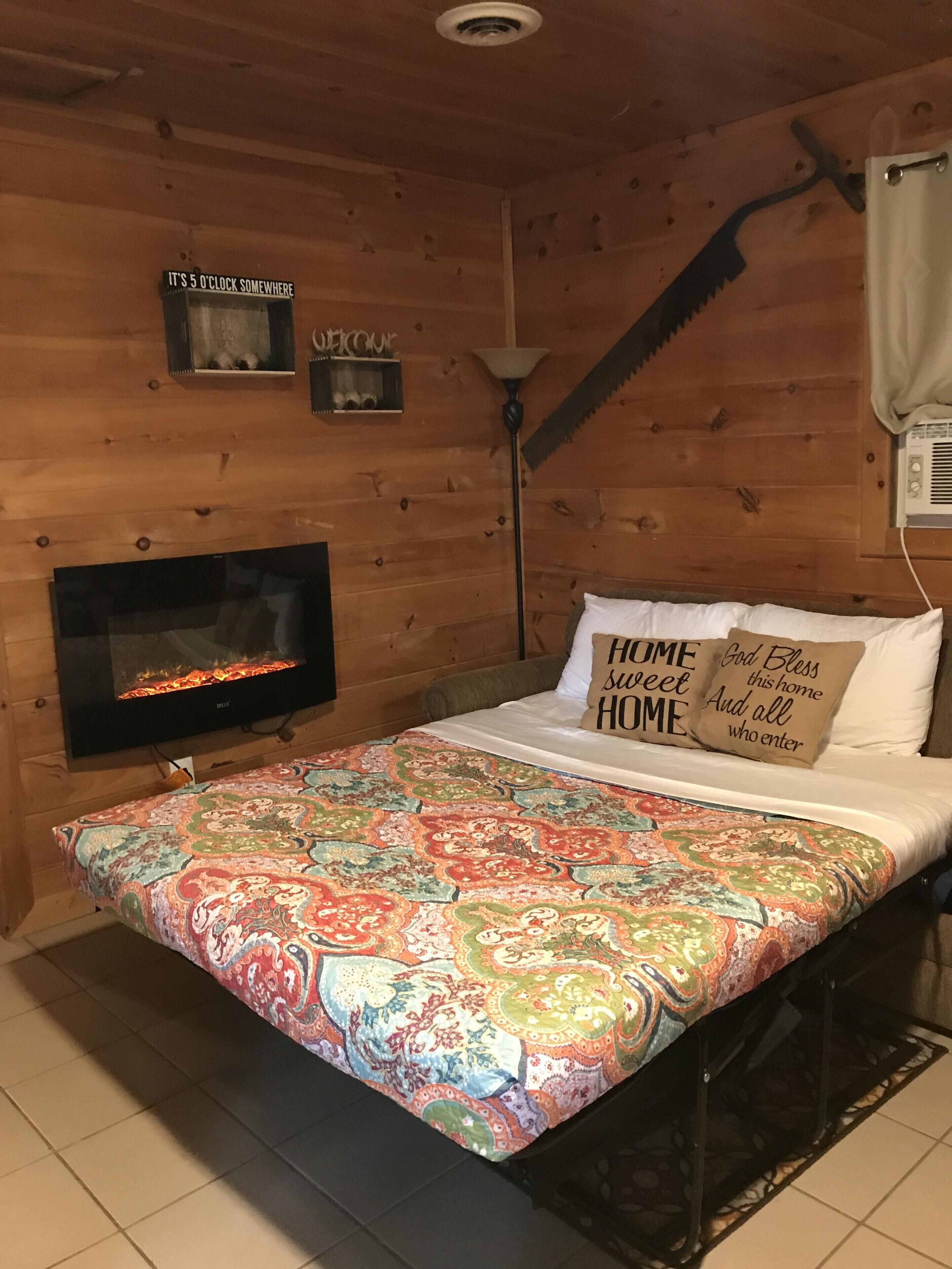 Ein gemütliches Zimmer mit Holzvertäfelung, einem Kamin, einem Bett mit gemusterten Textilien und einem an der Wand befestigten Fernseher.