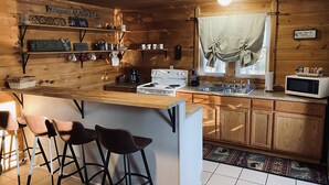 A cozy kitchen with wooden walls, a central island with stools, a stove, and a microwave. - 3 Bed Cozy Cabin Near Trails, Tippy Dam, Manistee River, Casino. (Wellston)