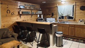 A cozy cabin-style kitchen with wooden walls, a bar area, and a dining space. - 3 Bed Cozy Cabin Near Trails, Tippy Dam, Manistee River, Casino. (Wellston)