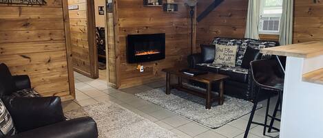 Een gezellig interieur van een blokhut, met een open haard, een bank, een salontafel en een eethoek.