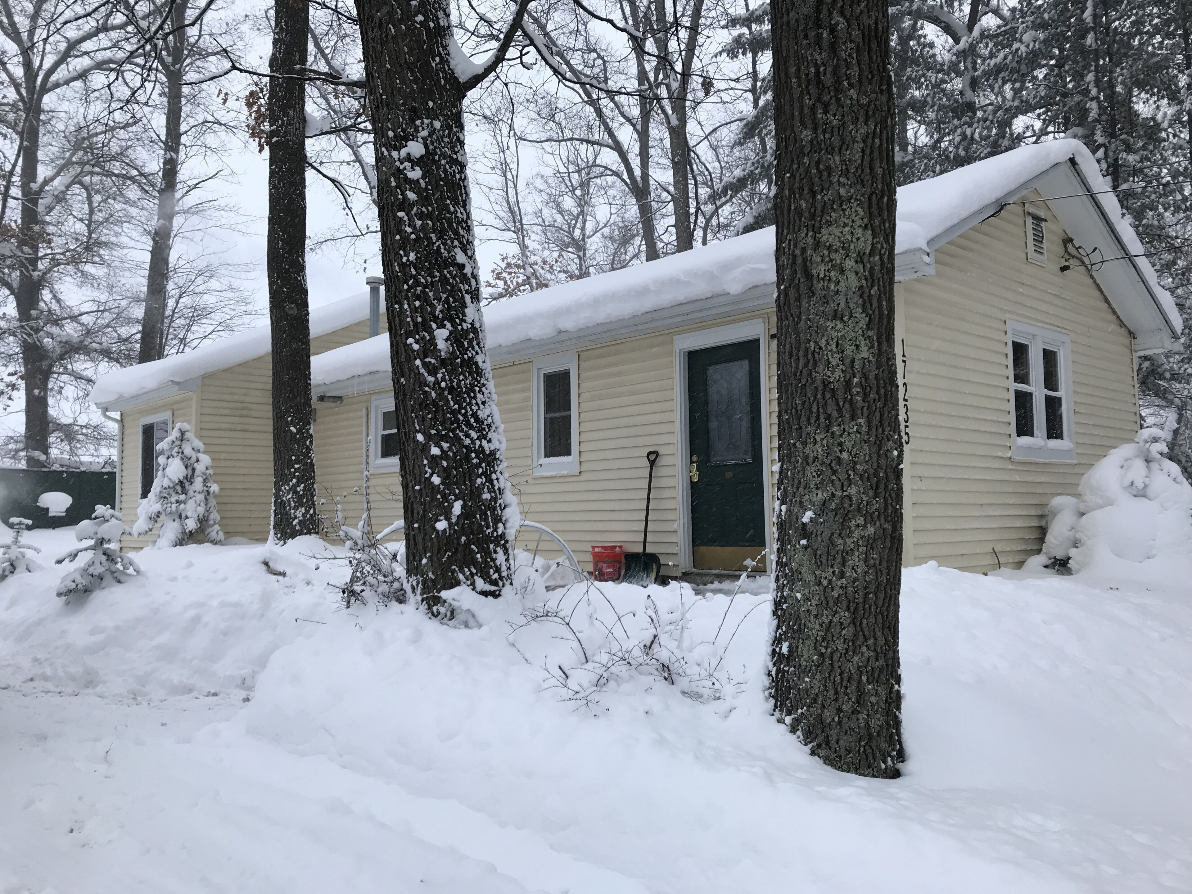 Una casa cubierta de nieve con puerta, ventanas y un cobertizo pequeño en un paisaje nevado.