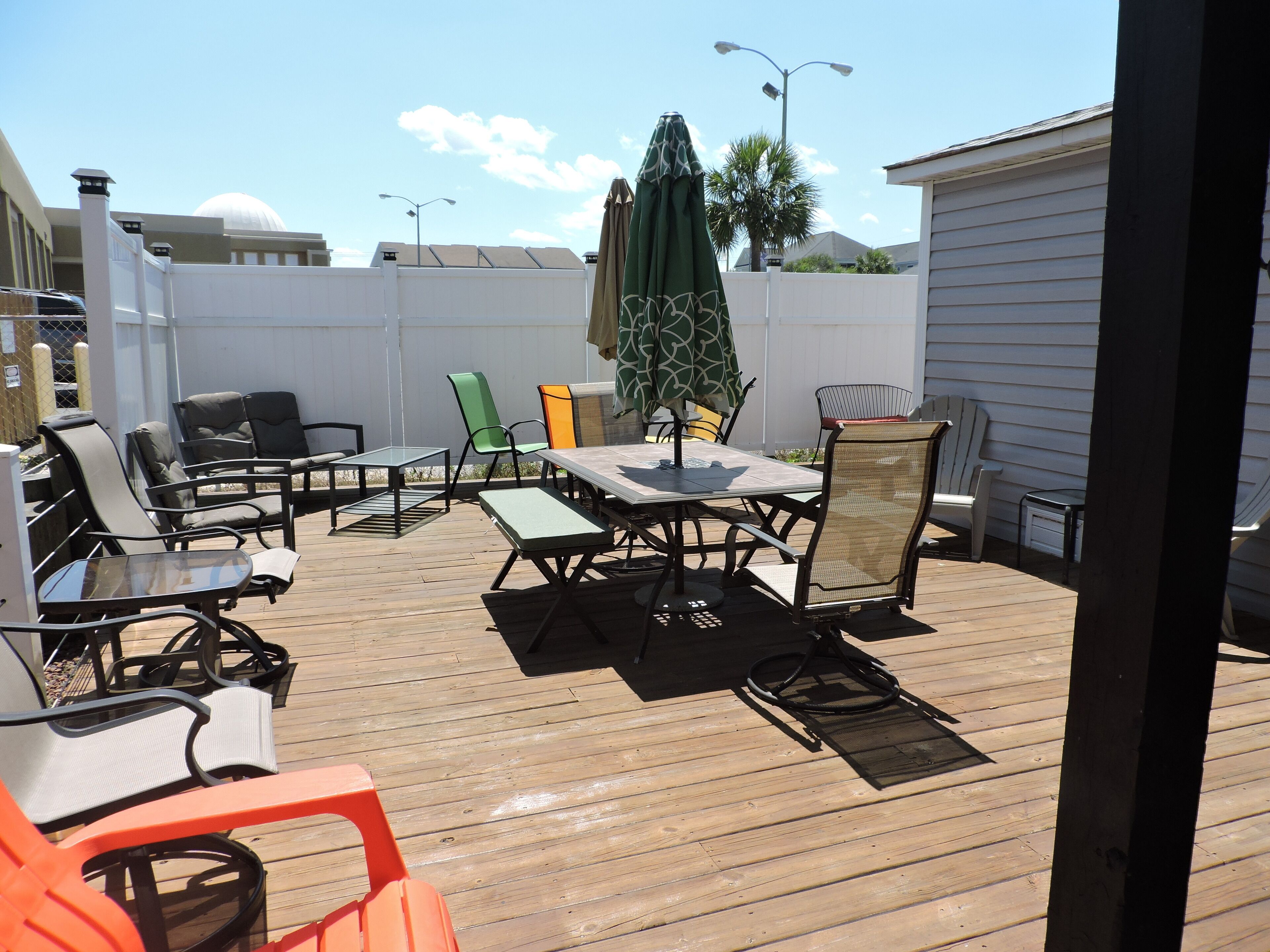 An outdoor deck with a table and chairs, a green umbrella, and a white fence.