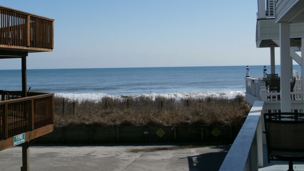 A view of the ocean from a balcony with a wooden railing and a concrete barrier.