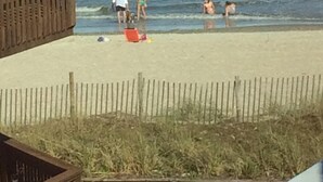 A beach with a wooden structure, a fence, and people near the water.