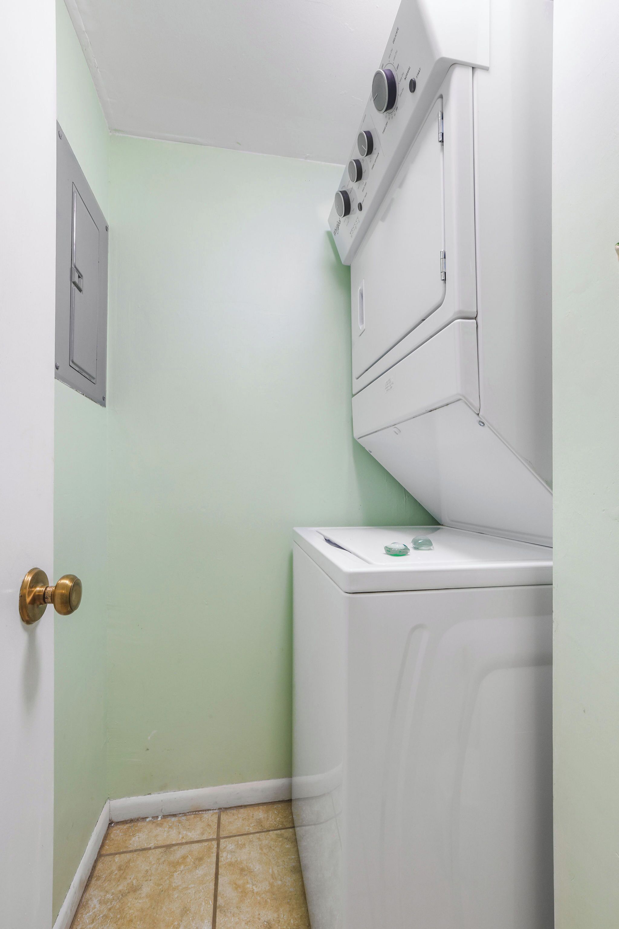 A laundry room with a washing machine and dryer, a door with a brass handle, and a light green wall.