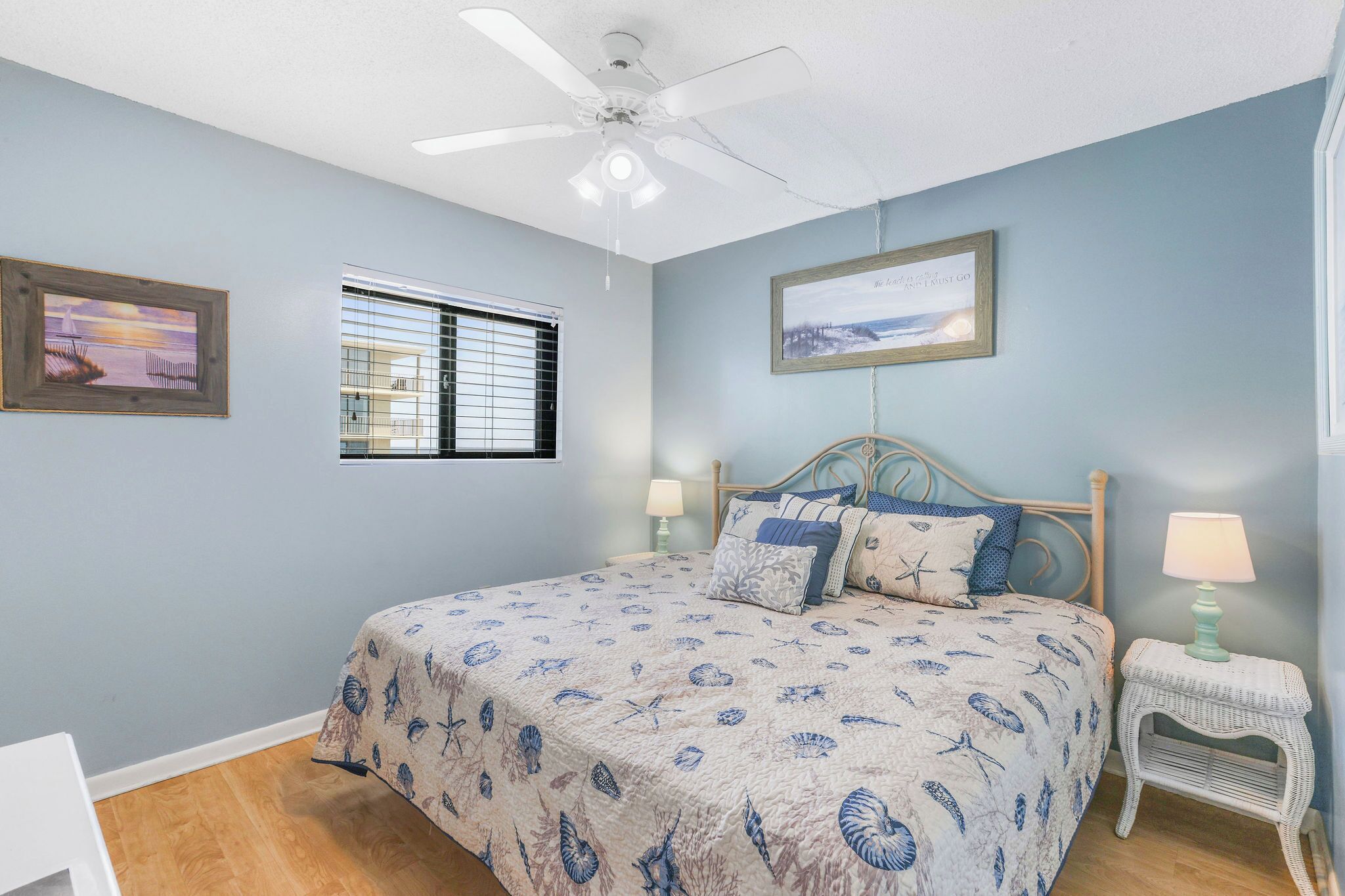 A bedroom with a bed, a ceiling fan, a window with blinds, and two wall-mounted lamps.