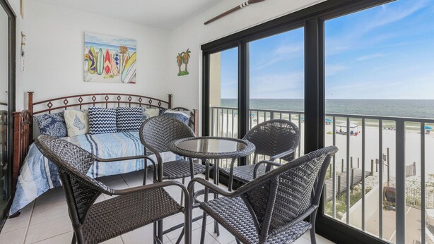 Un balcon agrémenté de meubles en osier, un lit avec une literie à motifs et un tableau représentant des planches de surf.