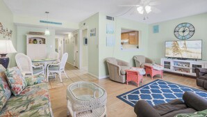 Un salon comprenant un canapé, des fauteuils, un téléviseur et un coin repas avec une table et des chaises.
