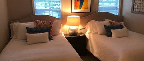 A hotel room with two beds, a nightstand with a lamp, and a framed artwork on the wall.