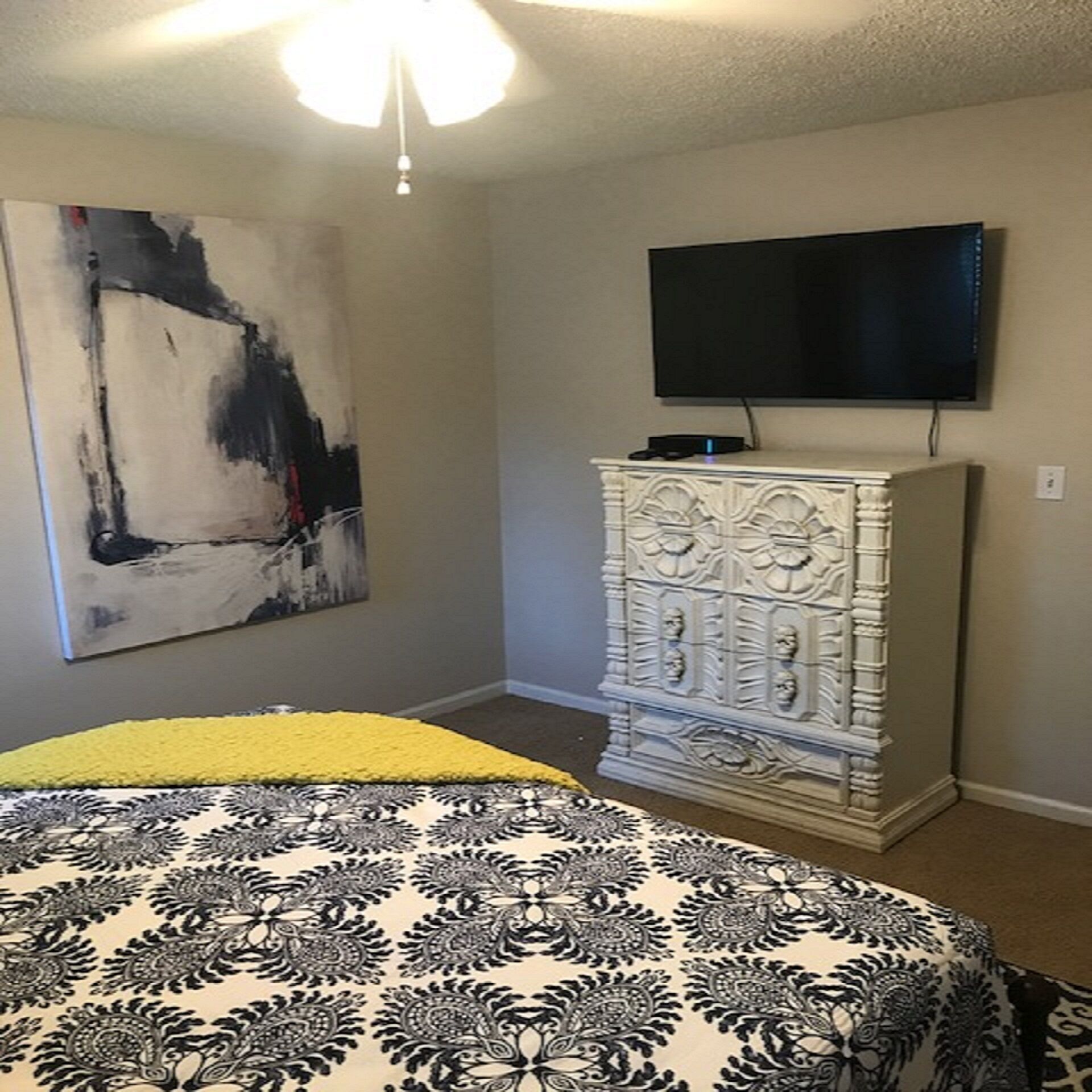 Un dormitorio con cama, cómoda, televisión y un cuadro en la pared.