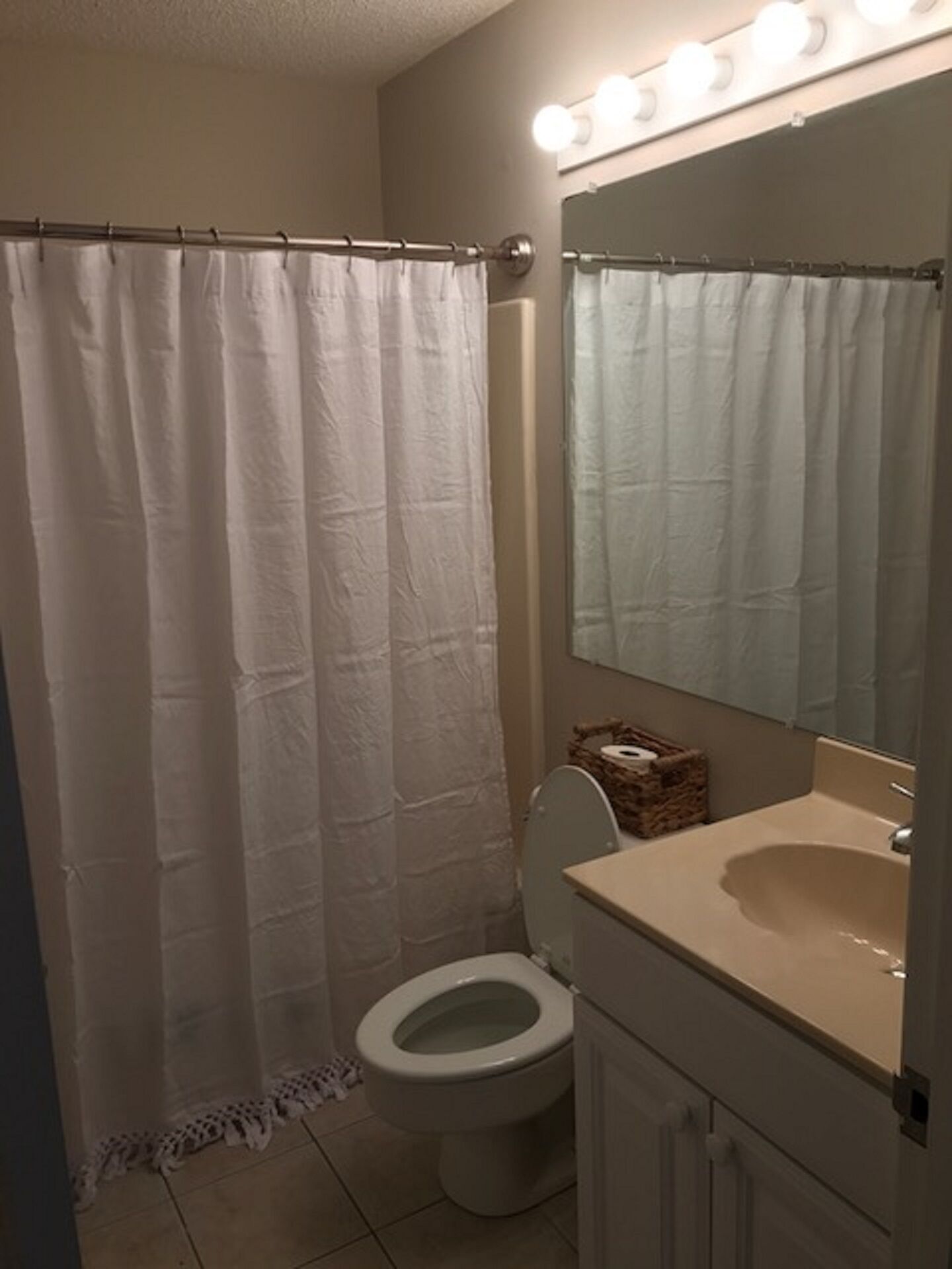 Een badkamer met douchegordijn, toilet, wastafel en een spiegel met verlichting erboven.