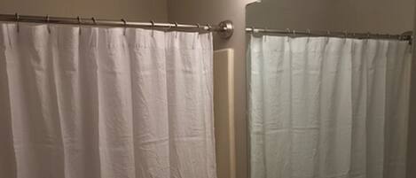 Een badkamer met douchegordijn, toilet, wastafel en een spiegel met verlichting erboven.