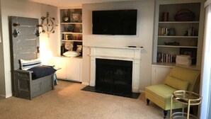 Un salon doté d’une cheminée, d’un téléviseur fixé au-dessus et d’une bibliothèque remplie de livres et d’objets décoratifs.